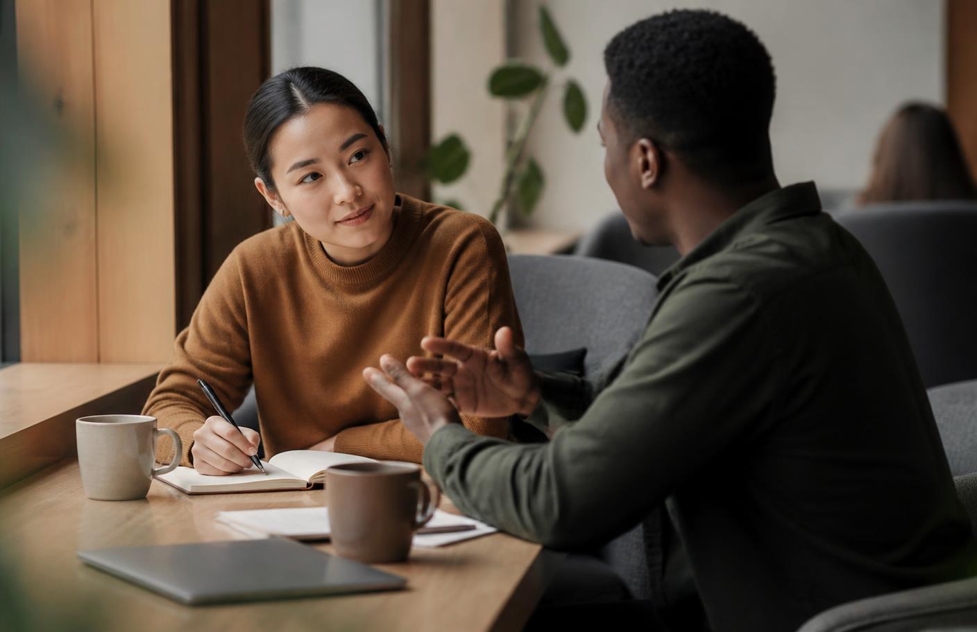 Two people talking over a notebook in a quiet coworking corner